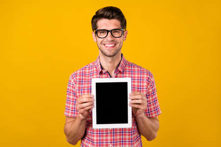 Portrait of attractive cheerful guy holding in hands tablet copy space isolated over bright yellow...