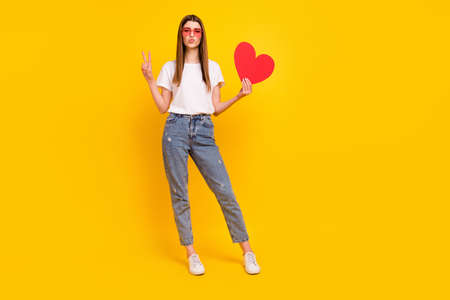 Full length photo of happy cheerful young woman make v-sign send air kiss red heart isolated on yellow color backgroundの写真素材
