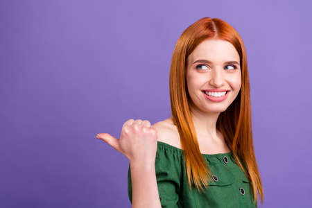 Photo of sweet pretty young lady wear green blouse pointing back looking empty space smiling isolated purple color backgroundの写真素材