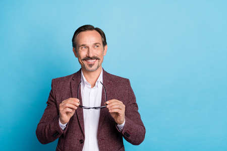 Photo of cheerful clever man take off eyewear look empty space wear red blazer isolated blue color backgroundの写真素材