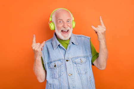 Photo of funny crazy man pensioner dressed retro denim vest earphones smiling showing hard rock sign...