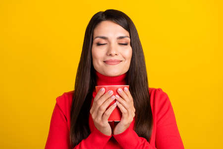 Photo of charming positive lady closed eyes hold cup nice scent inspiration isolated on yellow color backgroundの写真素材