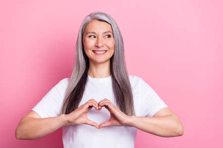 Photo portrait of aged woman with grey hair showing heart sign fingers isolated on pastel pink color...