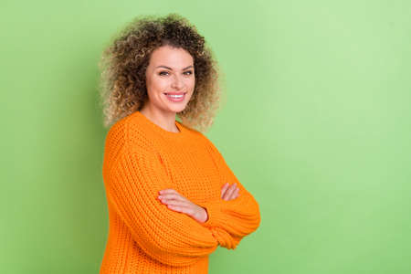 Photo of optimistic young blond lady crossed palms wear orange pullover isolated on green color backgroundの写真素材
