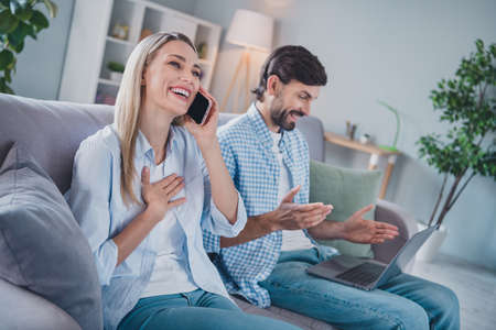 Photo of funny relaxed couple sit divan hold gadgets remote freelance wear casual outfit in comfortable home indoorsの写真素材