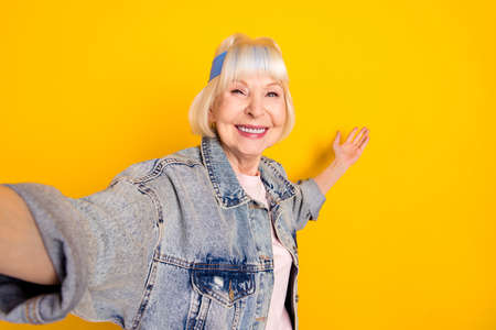 Photo portrait of senior woman smiling taking selfie showing blank space on hand isolated on vivid yellow color backgroundの写真素材