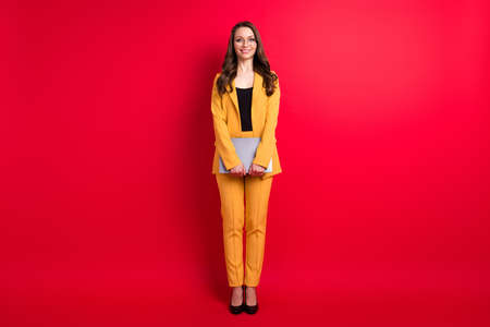 Full length body size view of attractive cheerful girl holding in hands laptop isolated over bright red color backgroundの写真素材