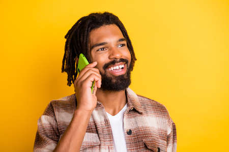Photo of attractive dark skin man dressed plaid shirt talking modern device looking empty space isolated yellow color backgroundの写真素材