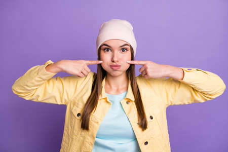 Portrait of optimistic straight hairdo girl puff cheeks wear cap jacket isolated on purple color...