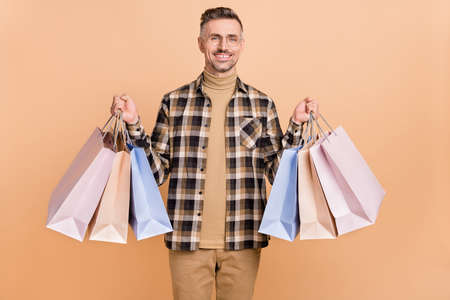 Photo of mature cheerful man hold shopping bag mall discount eyewear isolated over beige color...