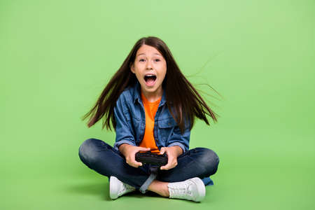 Full length photo of cool small girl play station yell wear shirt jeans shoes isolated on green backgroundの写真素材