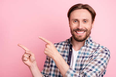 Photo of young man happy positive smile indicate fingers empty space subscribe recommend advise isolated over pink color backgroundの写真素材