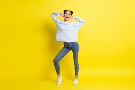 Photo of positive lady dance hands face look empty space wear blue pullover jeans sneakers isolated yellow backgroundの写真素材