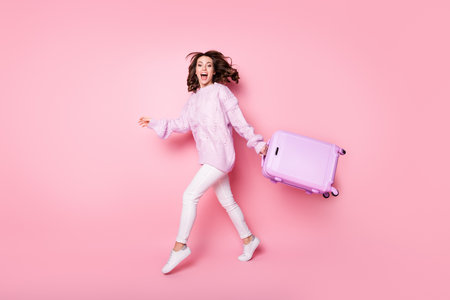 Photo of shiny funny young woman knitted sweater running holding suitcase isolated pastel pink color backgroundの写真素材