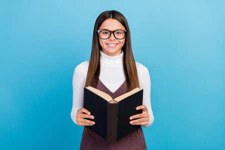 Photo of young school girl pupil eyewear read book materials homework isolated over blue color...