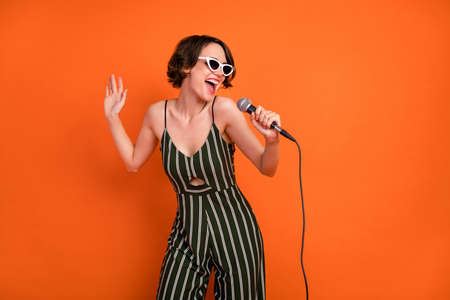 Photo of young attractive girl happy positive smile sing microphone karaoke isolated over orange color backgroundの写真素材