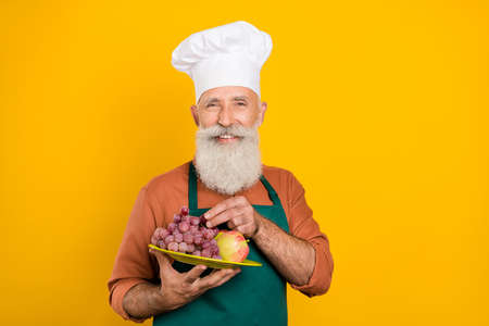 Portrait of attractive cheery grey-haired man chef eating snack fresh berries cafe cafeteria...