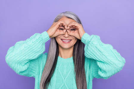 Photo of cheerful senior woman show finers eyeglasses binoculars watch isolated over violet color...