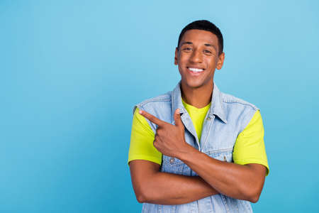 Photo of young afro man promoter indicate finger empty space choose recommendation isolated over blue color backgroundの写真素材