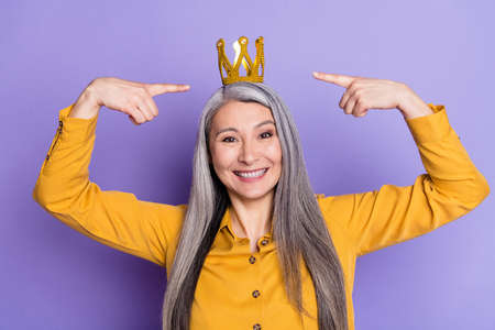 Portrait of nice elderly retired cheerful woman demonstrating crown charisma wealth isolated on bright violet purple color backgroundの写真素材