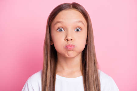 Close-up portrait of attractive funny preteen girl holding air in cheeks fooling isolated over pink...