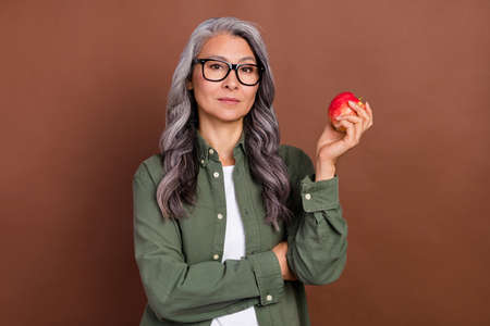 Photo of good elder grey hairdo lady hold apple wear shirt eyesight isolated on brown color backgroundの写真素材