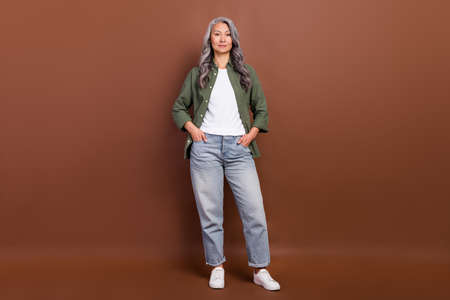 Full size photo of cool old white hairdo lady stand wear khaki shirt jeans sneakers isolated on...