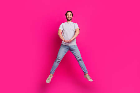 Photo of funny handsome guy jump hold hands wear striped t-shirt jeans footwear isolated pink color backgroundの写真素材