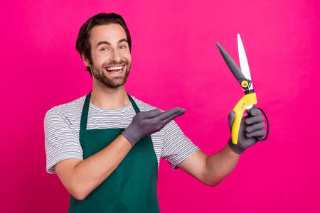 Photo of florist shop owner man palm demonstrate shears wear gloves apron t-shirt isolated pink color backgroundの写真素材