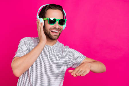 Photo of young man hand touch headphones wear glasses look empty space party isolated over magenta...