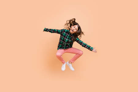 Photo of funny pretty schoolgirl wear plaid outfit jumping high arms sides smiling isolated beige color backgroundの写真素材