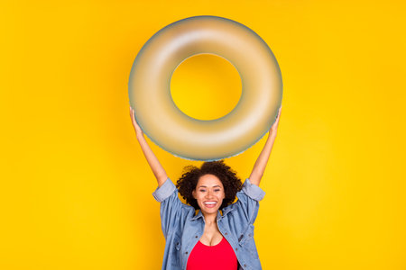Photo of young happy positive afro american woman hold hands rubber circle isolated on yellow color backgroundの写真素材