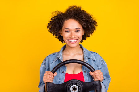 Photo of young positive afro american happy woman hold hands steering wheel isolated on yellow color...
