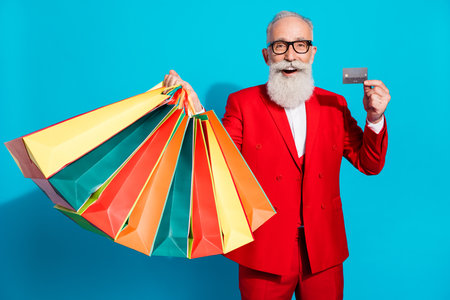 Photo portrait aged man in glasses showing bank card keeping packages isolated bright blue color backgroundの写真素材