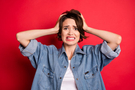 Photo of sad brunette young lady hands head wear jeans shirt isolated on red color background