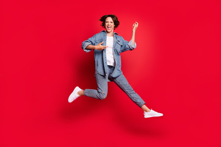 Full size photo of young woman happy positive smile play guitar jump isolated over red color backgroundの写真素材