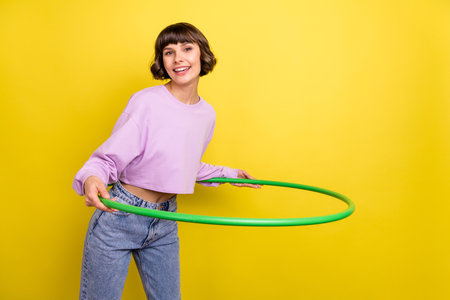 Portrait of attractive cheerful girl doing exercise with ring copy space isolated over bright yellow color backgroundの写真素材