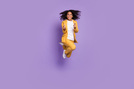 Photo of cheerful positive lady wear yellow suit glasses jumping high pointing fingers you isolated purple color backgroundの写真素材
