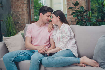 Portrait of attractive careful gentle cute dreamy couple cuddling spending time sitting on divan...