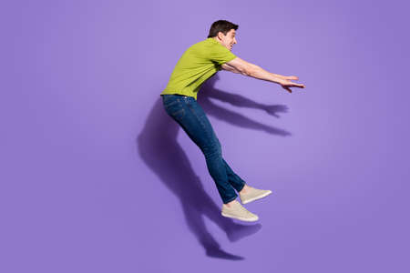 Photo of handsome funny young guy dressed green t-shirt smiling jumping high isolated purple color backgroundの写真素材