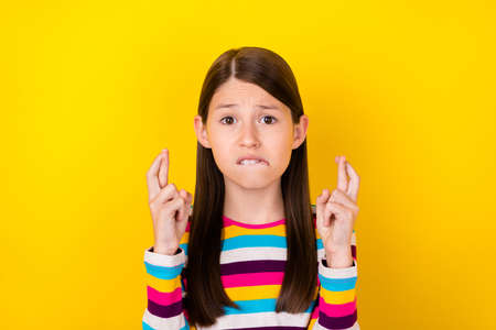 Photo of nervous small lady crossed fingers bite lip pray exam result wear striped shirt isolated...