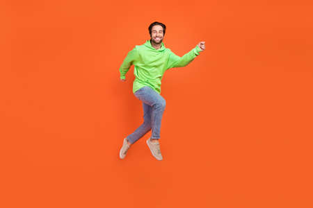 Full body photo of brunet young guy run wear sweatshirt jeans sneakers isolated on orange background