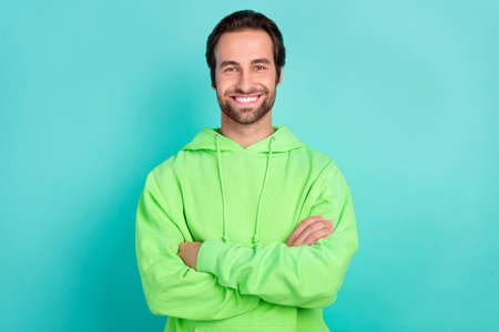 Photo of positive self-assured guy crossed hands toothy smile wear green hoodie isolated teal color backgroundの写真素材