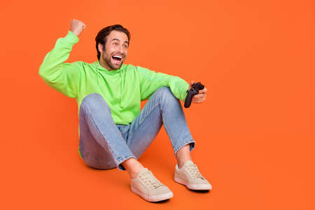 Full length photo of brunet young guy play station sit look promo wear green sport cloth jeans...