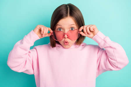 Photo of brunette hairdo impressed little girl hold eyewear wear pink sportswear isolated on teal color backgroundの写真素材