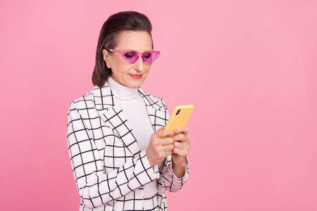 Photo of calm peaceful businesswoman in funky glasses using smartphone mobile isolated on pink color...