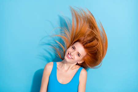 Portrait of attractive cheerful girl having fun throwing shine hair isolated over bright blue color backgroundの写真素材