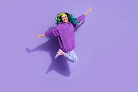 Full length photo of cheerful lady jump up imagine flying bird hold arms wings isolated over purple color backgroundの写真素材