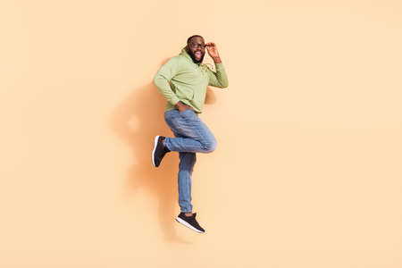 Full body profile portrait of cheerful active handsome guy hand touch spectacles isolated on beige color backgroundの写真素材