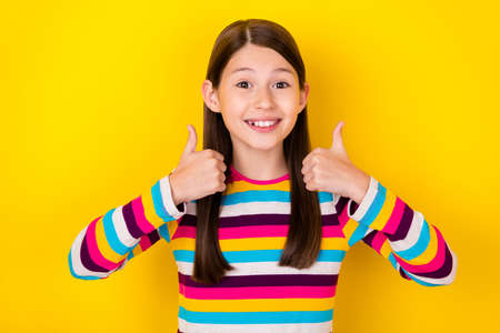 Photo of positive little lady raise thumbs up give positive feedback wear striped shirt isolated yellow color backgroundの写真素材